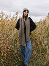 Woman wearing a brown knit cardigan, Cozy Earth Cable Knit Scarf stands in a field of tall grass |Color:Ash