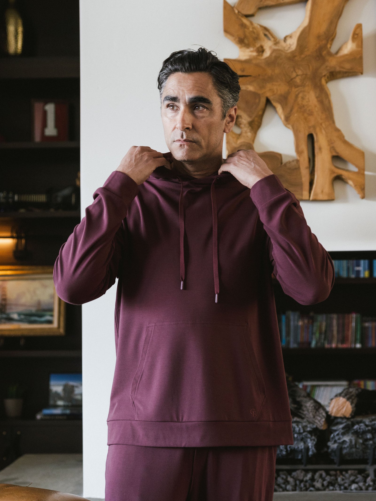 Burgundy Bamboo Hoodie worn by man standing in a living room of a house. The man is adjusting the hood of the hoodie