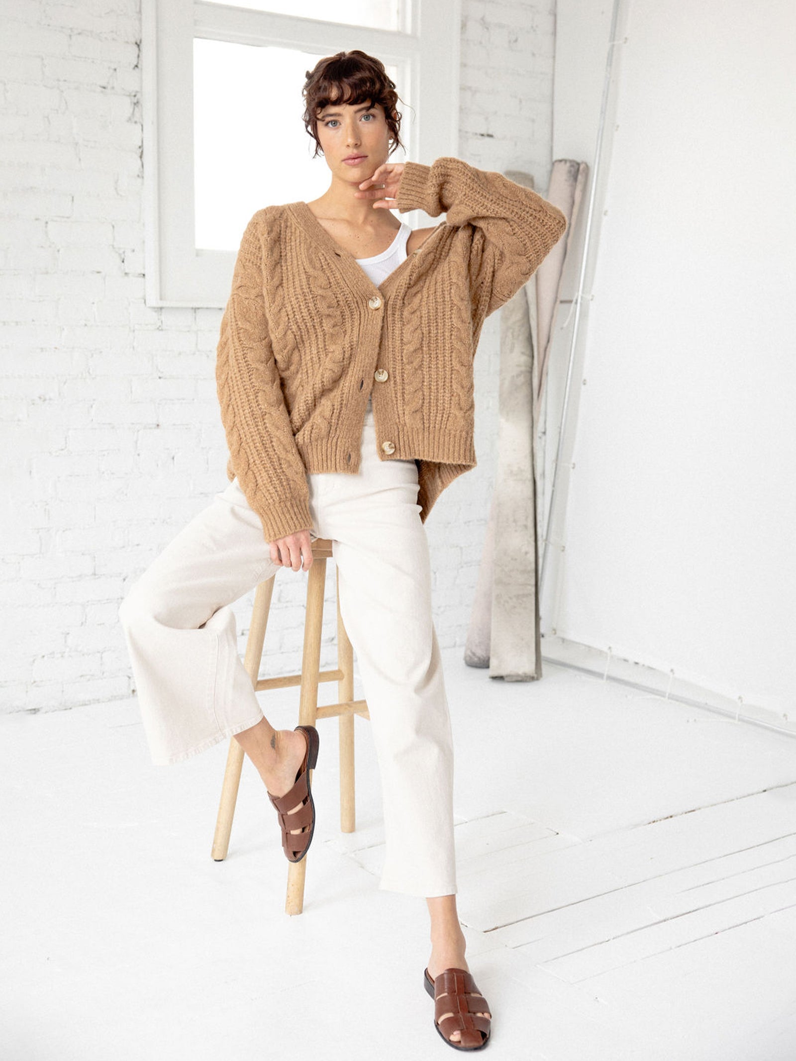 Woman sitting on wooden stool wearing camel cardigan