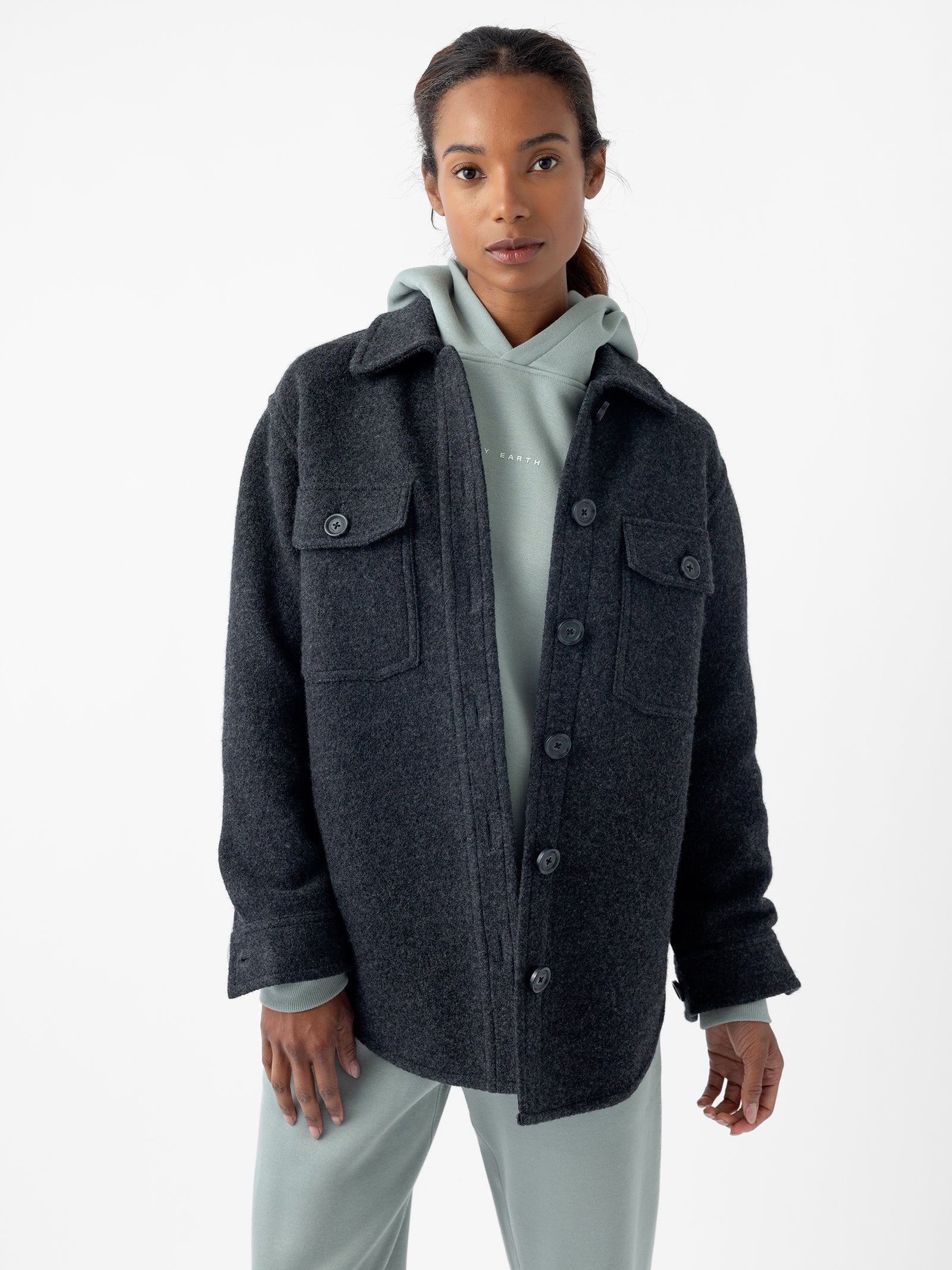 A person with long hair tied back is wearing the Women's Boucle Shacket by Cozy Earth, buttoned up over a light gray hoodie. They are standing against a plain white background, looking directly at the camera with a neutral expression.