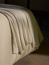 Creme Classic Knit Blanket draped over a bed in the sunlight. |Color:Creme