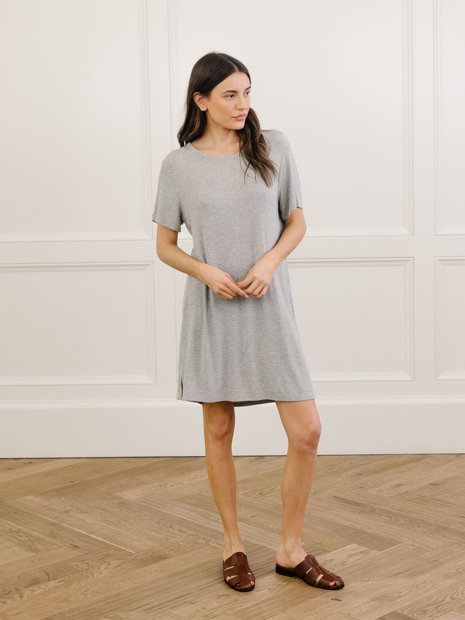 A woman standing in a grey Cozy Earth bamboo rib-knit boyfriend sleep dress with short sleeves, knee-length, in a lounge or bedroom setting.