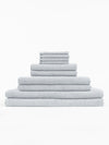 The Cozy Earth Complete Nantucket Bath Bundle features light gray textured towels in assorted sizes, neatly stacked in a pyramid formation against a plain white background.|Color: Heathered Harbor Mist