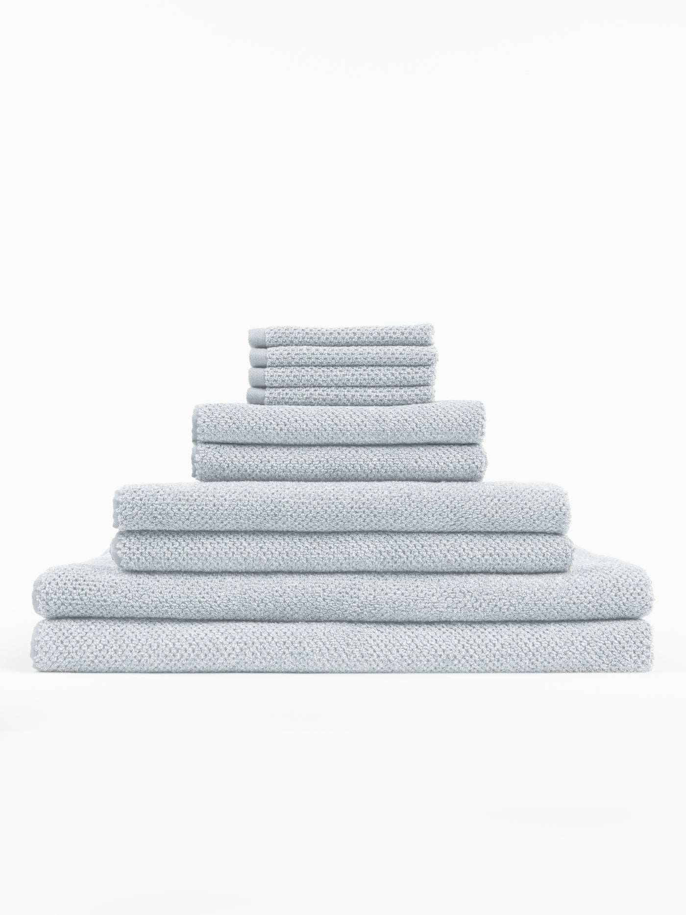 The Cozy Earth Complete Nantucket Bath Bundle features light gray textured towels in assorted sizes, neatly stacked in a pyramid formation against a plain white background.|Color: Heathered Harbor Mist