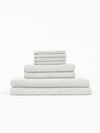 The Cozy Earth Nantucket Bath Towel Set features textured, light gray towels in assorted sizes, neatly stacked on a white background.|Color:Heathered Light Grey
