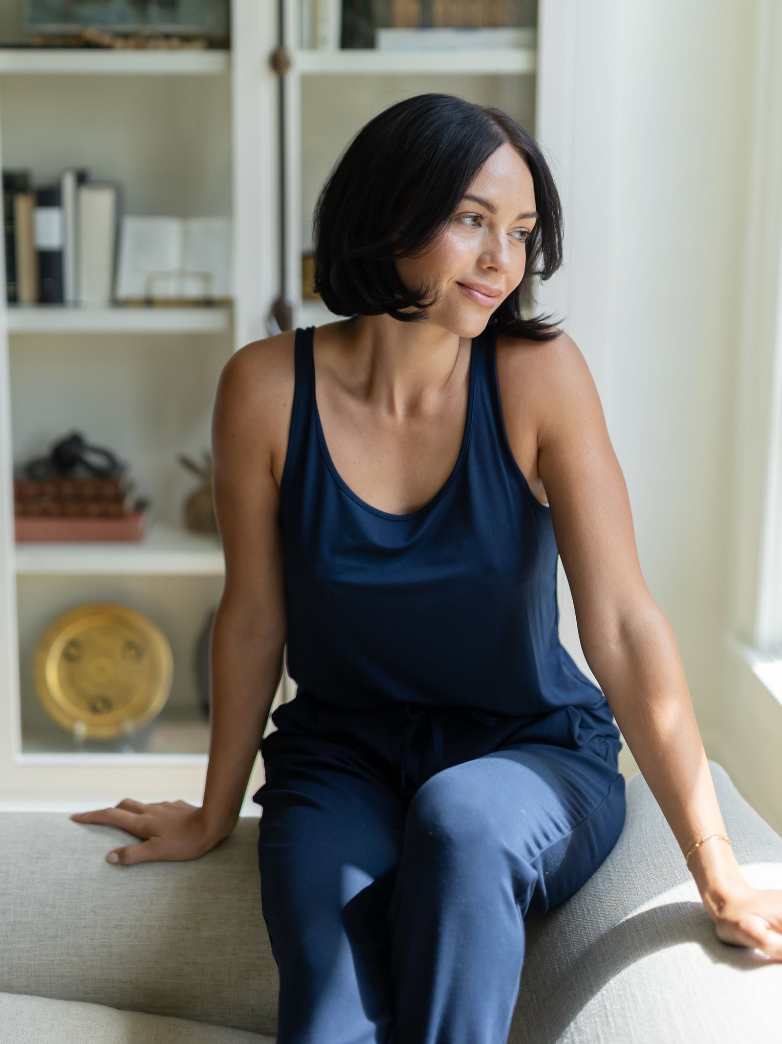 A woman sitting in a relaxed pose wearing a navy blue Cozy Earth bamboo stretch-knit lounge tank top and matching pants.