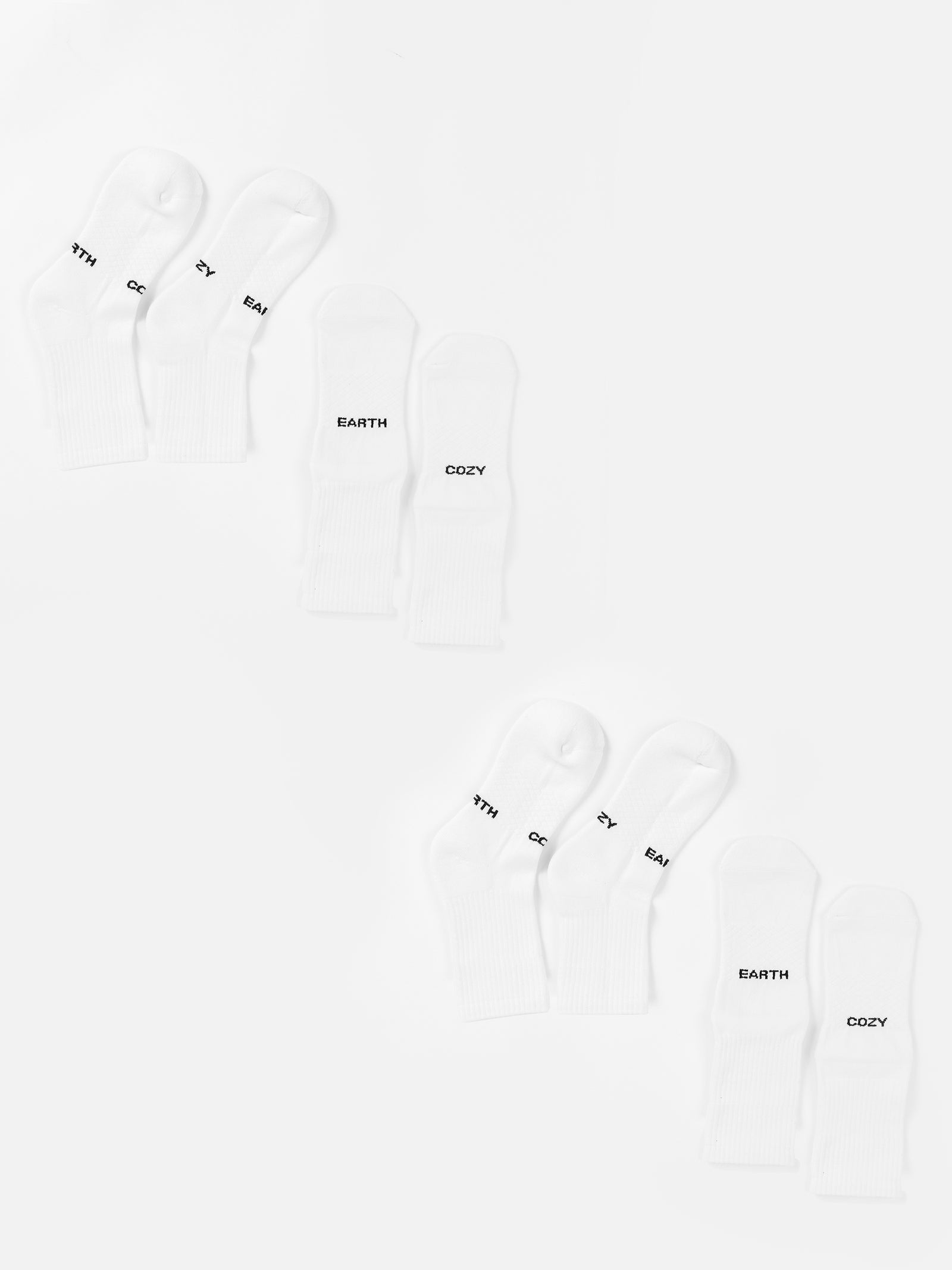 Two sets of three pairs of white Essential Calf Sock 4-Packs from Cozy Earth are arranged in two rows on a white background. Each sock is labeled with the words "MYTH," "EARTH," or "COZY" in black text near the toes. The arrangement is neat, with one set of socks mirroring the other.