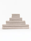 The Complete Nantucket Bath Bundle by Cozy Earth, featuring beige textured towels in various sizes, is neatly stacked pyramid-style on a white background.|Color:Heathered Sand
