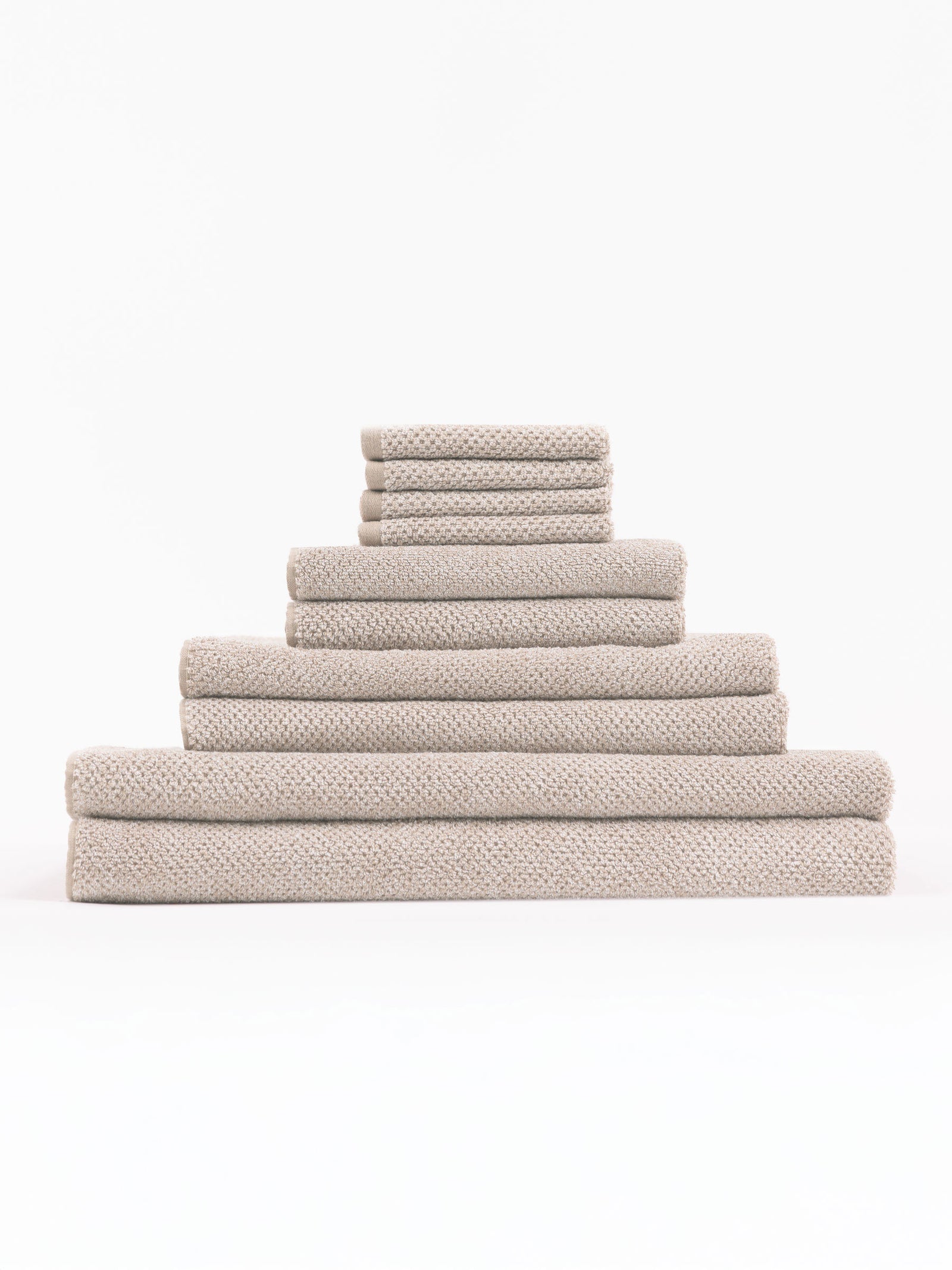 The Complete Nantucket Bath Bundle by Cozy Earth, featuring beige textured towels in various sizes, is neatly stacked pyramid-style on a white background.