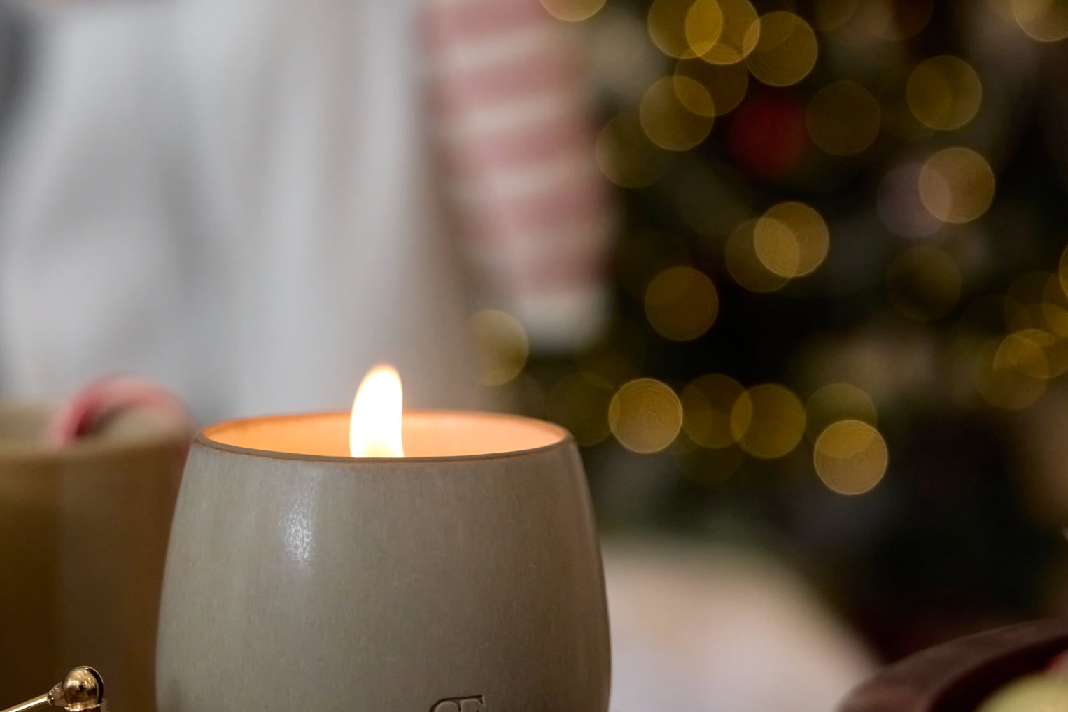 Candle in a ceramic holder with a blurred Christmas tree in the background