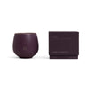 A deep purple Cozy Earth Candle EVOKE in a rounded cup with "CE" embossed on the front sits beside a matching purple box labeled "Evoke." Size: 9.2 oz (260 g).