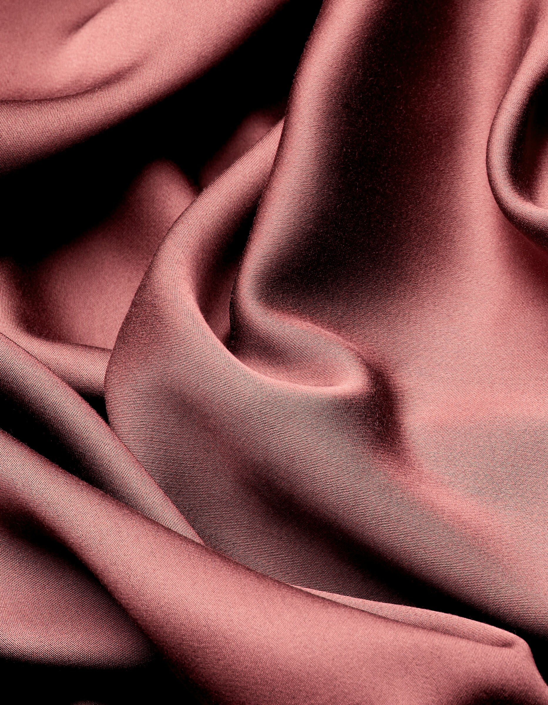Smooth, shiny Bamboo Sheet Set by Cozy Earth drapes in soft, flowing folds, creating elegant highlights and shadows across the rose-colored satin surface.|Color:Mulberry