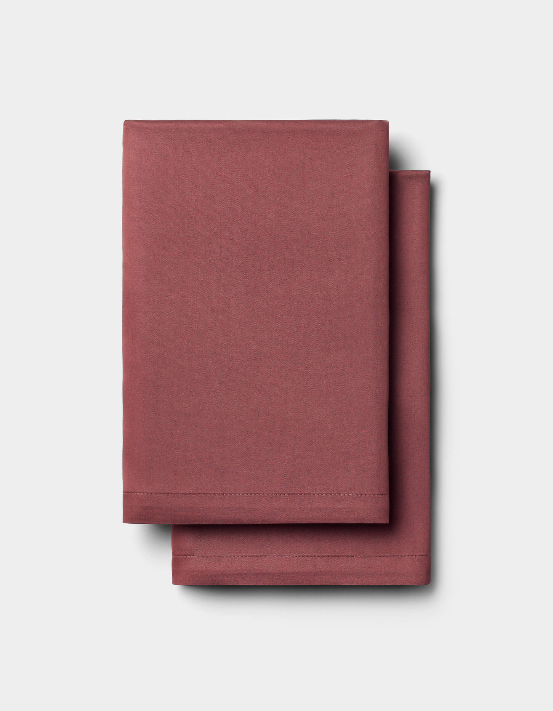 Two folded, solid maroon Bamboo Sheet Sets by Cozy Earth are stacked neatly on a plain light gray background.|Color:Mulberry
