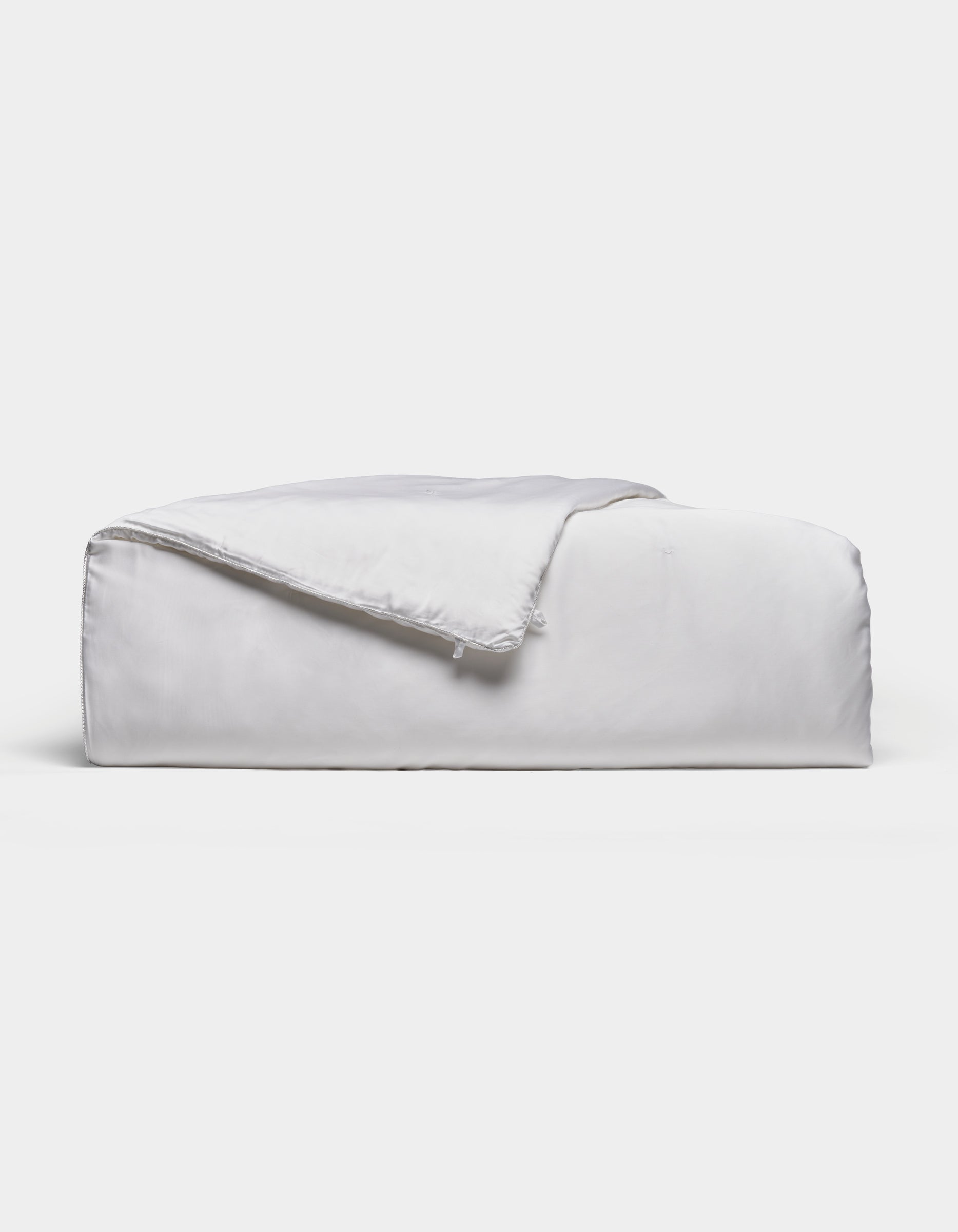 A neatly folded, fluffy Silk Comforter by Cozy Earth is placed against a plain light background. The fabric appears smooth and soft, highlighting its plush and inviting texture.|Filling:Extra