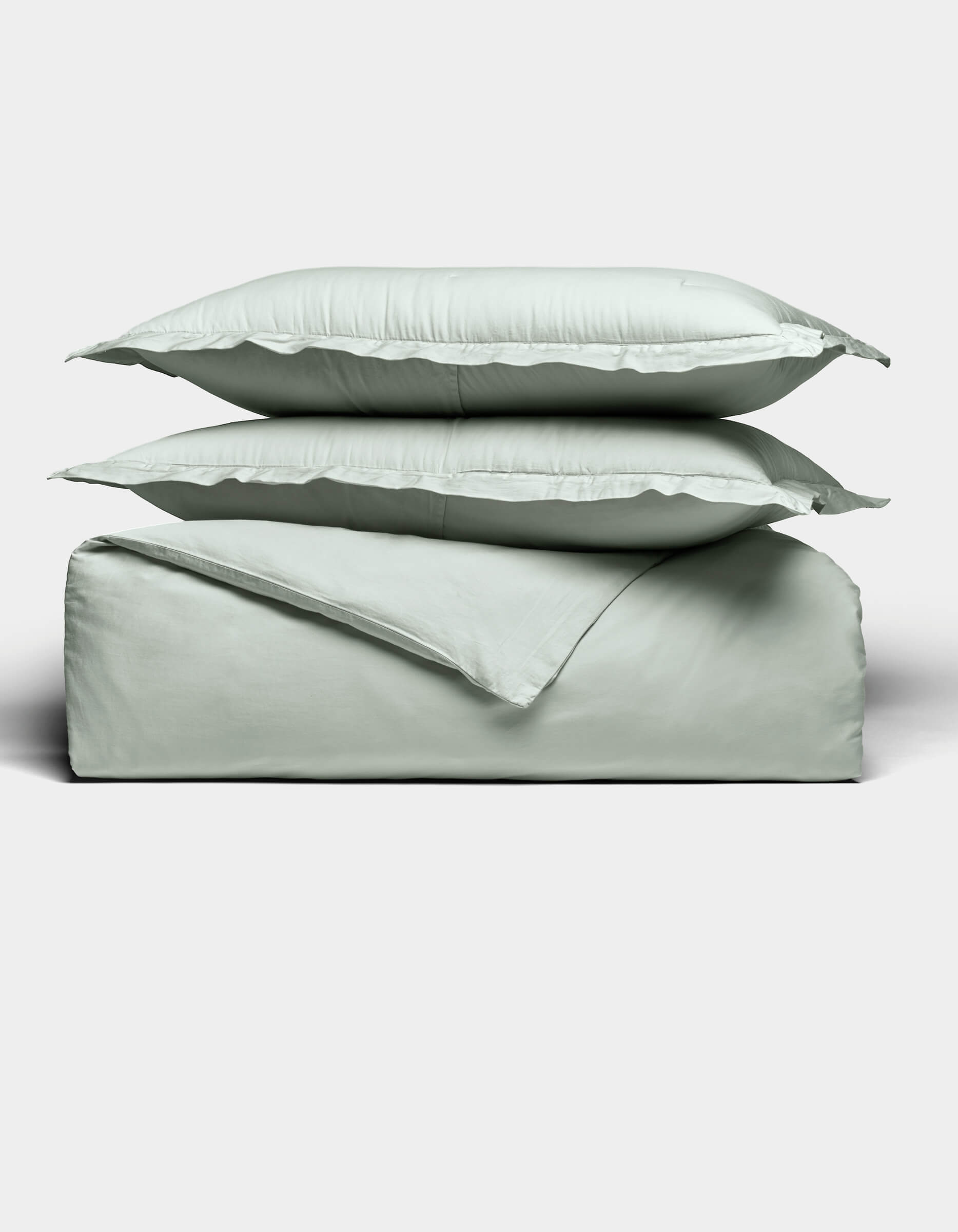 Two light gray pillows are stacked atop a matching folded Soft-Wash Cotton Duvet Set by Cozy Earth, all set against a plain white background. The bedding appears soft and smooth, highlighting its cozy and minimal aesthetic.|Color:Laurel
