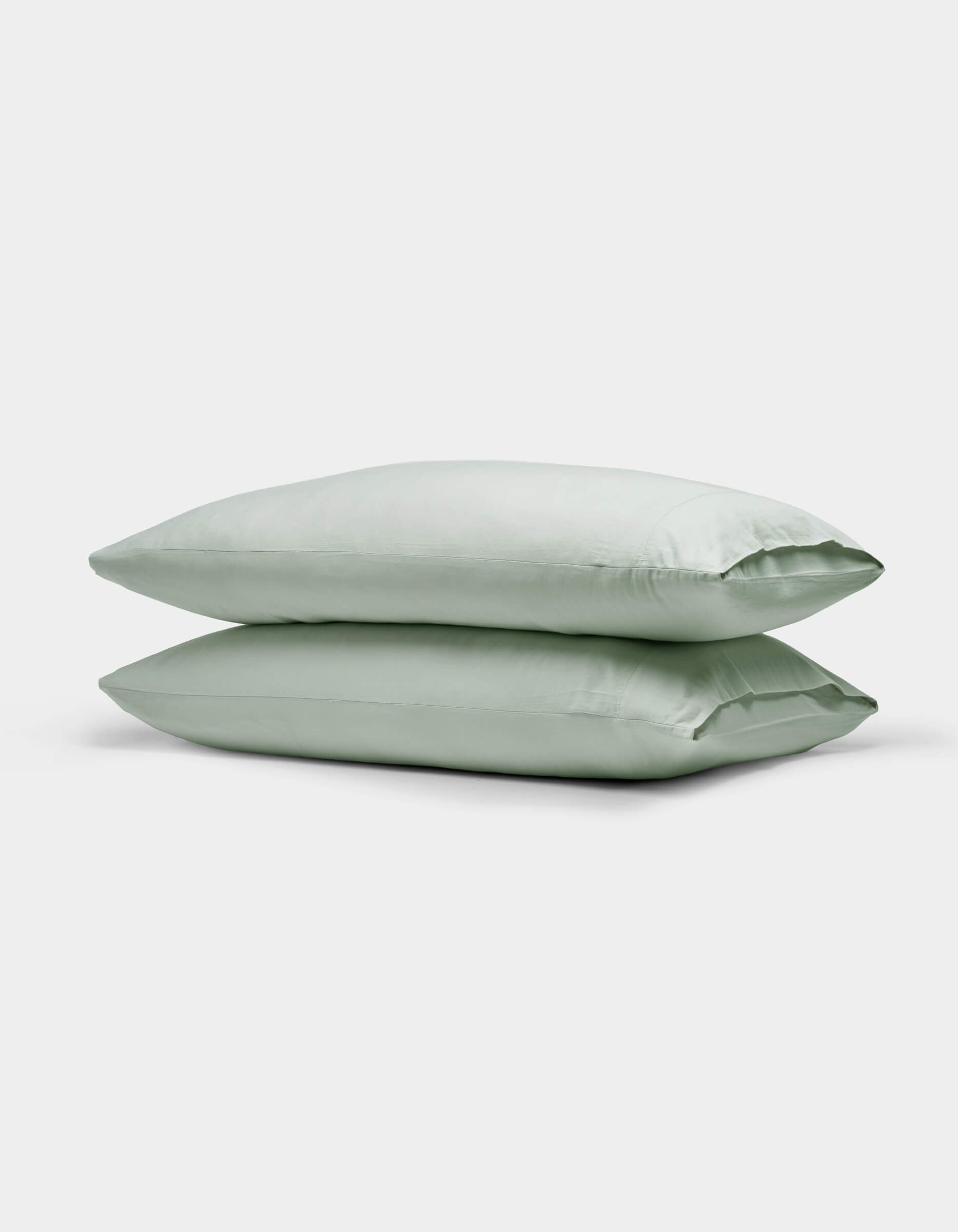 Two Cozy Earth Soft-Wash Cotton Pillowcases in light green are neatly stacked against a plain white background.|Color:Laurel