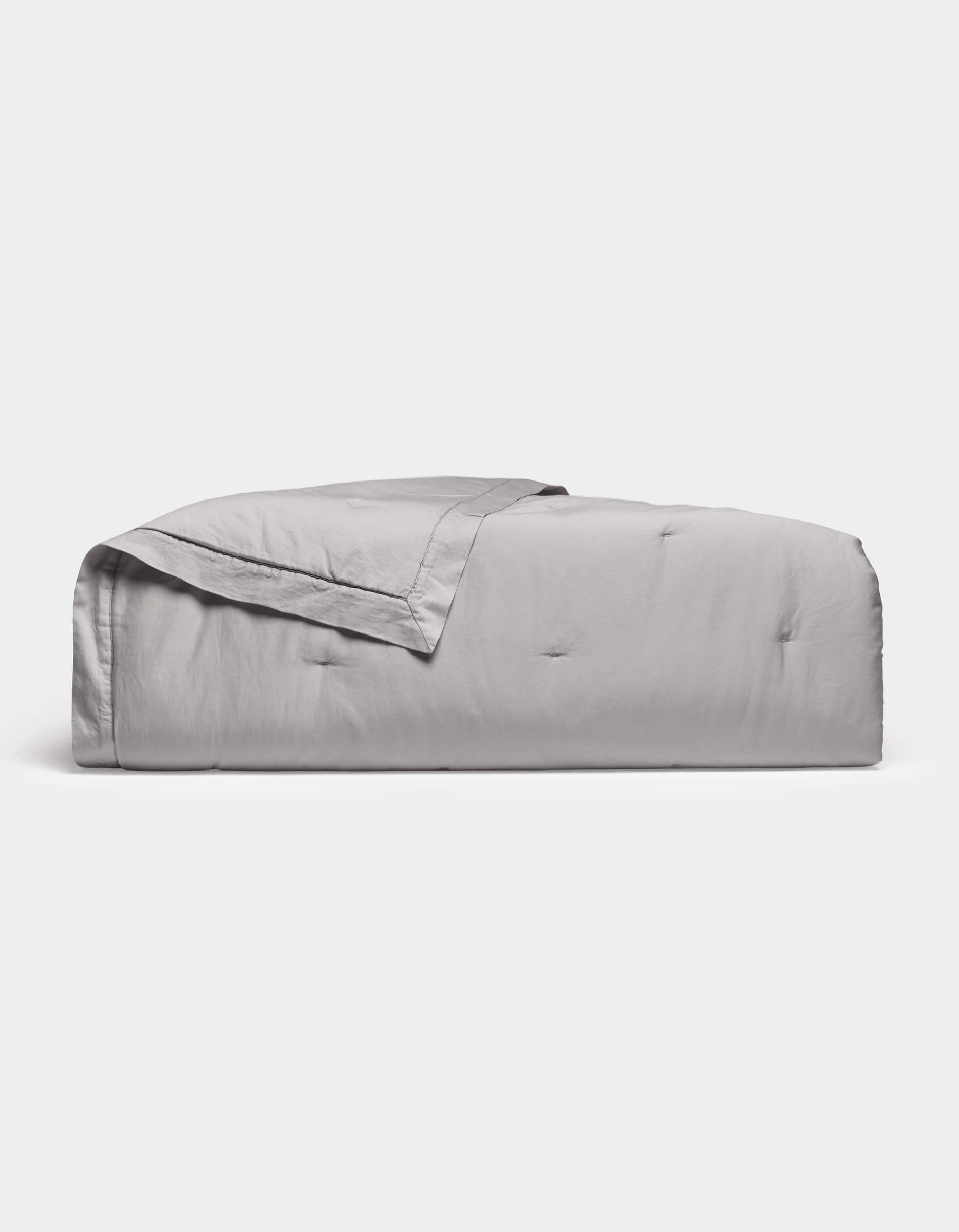 The Cozy Earth Soft-Wash Cotton Quilt in light gray features a subtle quilted pattern and is neatly folded, displayed against a plain white background.|Color:Dew