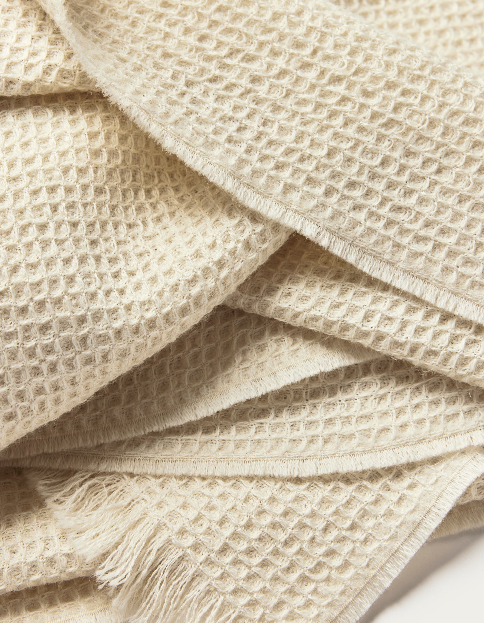 A close-up of the Cozy Earth Alpaca Waffle Throw highlights its cream-colored waffle weave texture and fringed edges, showcasing its soft and cozy appearance.