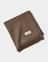 A folded brown Alpaca Waffle Throw by Cozy Earth with fringed edges and a small rectangular "Cozy Earth" label, displayed on a plain white background.|Color:Ebony