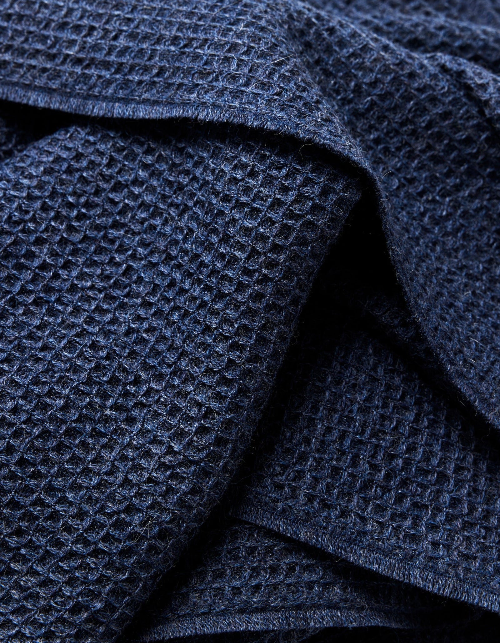 Close-up of the Cozy Earth Alpaca Waffle Throw in dark blue, showing its waffle-textured fabric with overlapping folds that emphasize the raised grid pattern and soft appearance.