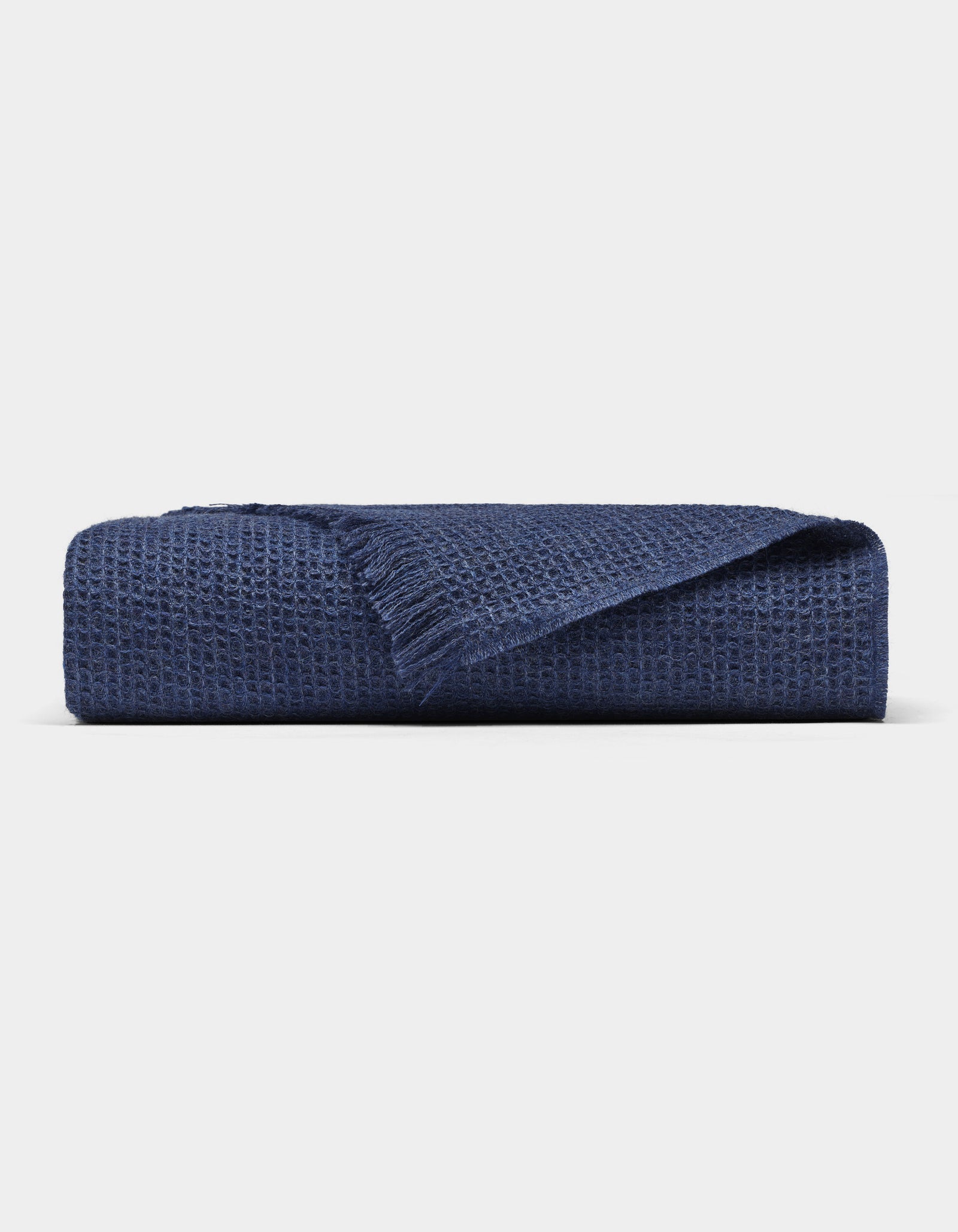 The Cozy Earth Alpaca Waffle Throw, in navy blue with a waffle texture and fringed edge, is shown folded against a plain light background.
