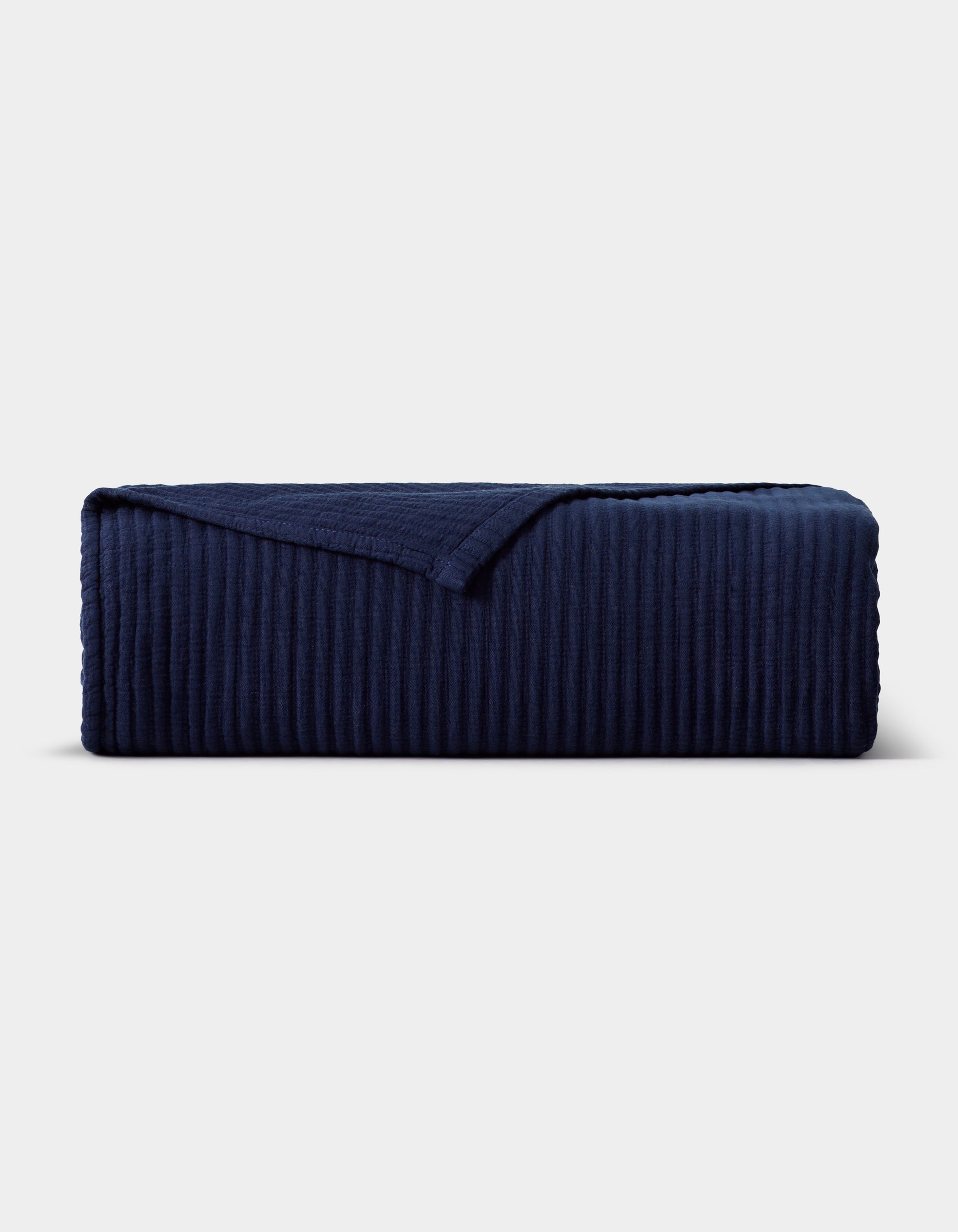 The Cozy Earth Bamboo Coverlet, in dark navy blue with a ribbed texture and one corner turned down, is displayed neatly against a plain light gray background.|Color:Navy