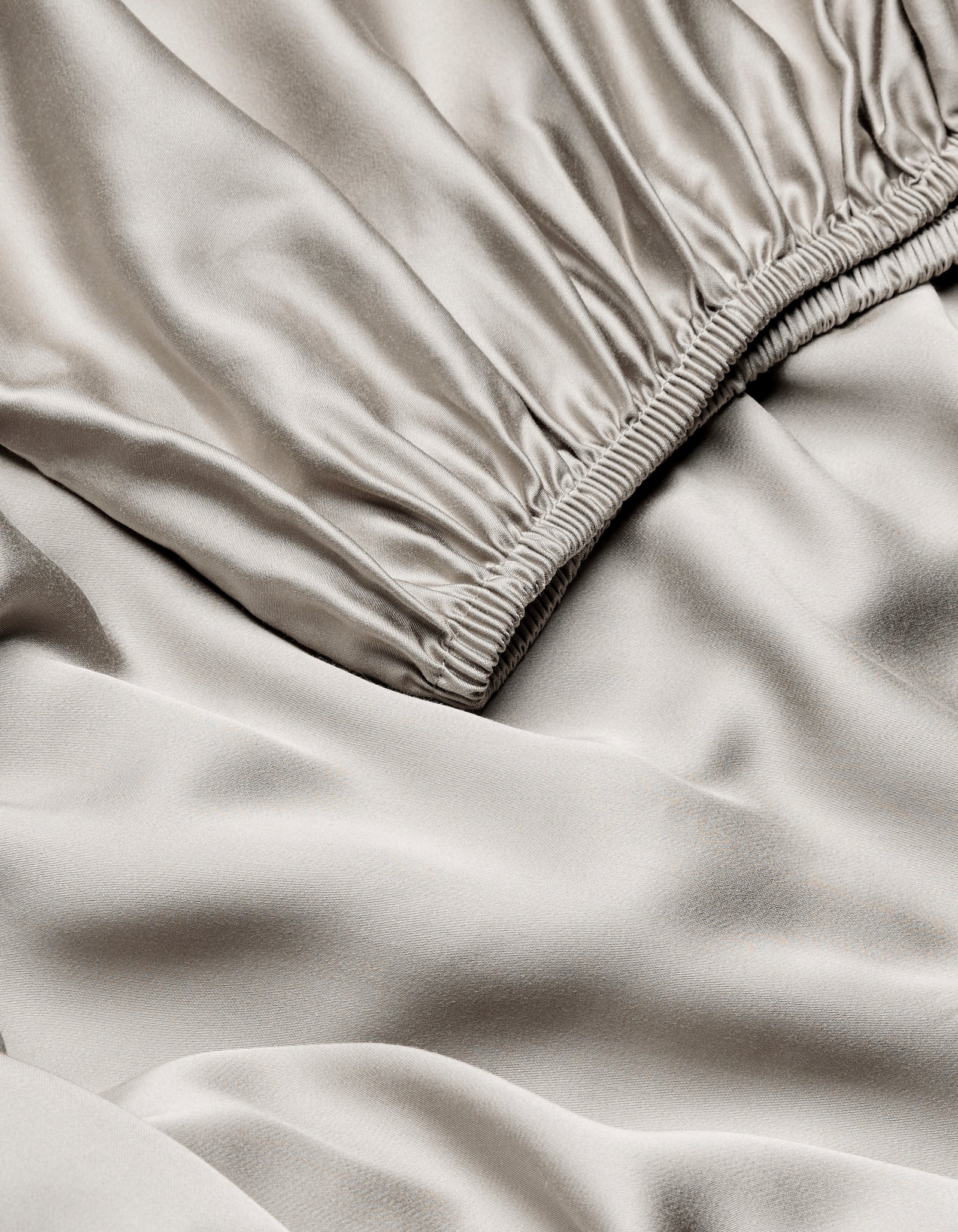 Close-up of Cozy Earth Bamboo Fitted Sheet in light beige, highlighting its smooth, shiny texture with gentle folds and ruching near the seam.