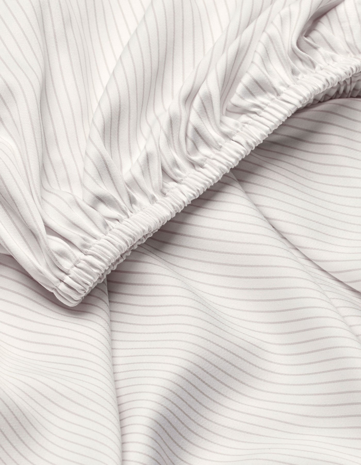 Close-up of Cozy Earth Bamboo Fitted Sheet: light-colored, finely striped fabric with gentle folds and elastic seam, creating a softly textured surface.