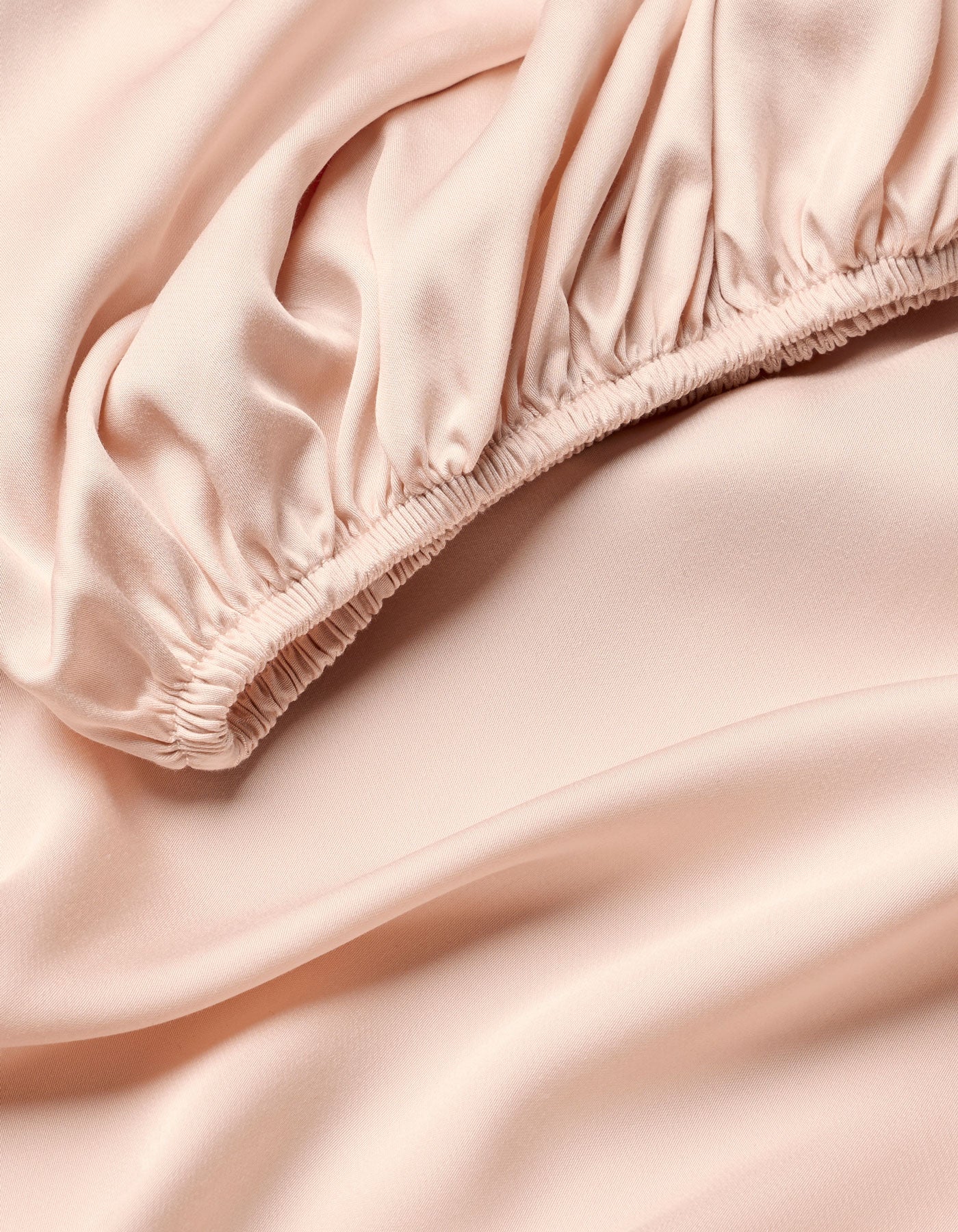 Close-up of Cozy Earth Bamboo Fitted Sheet in pale pink, featuring soft, flowing folds and gathered elastic detail for a smooth, shiny texture.