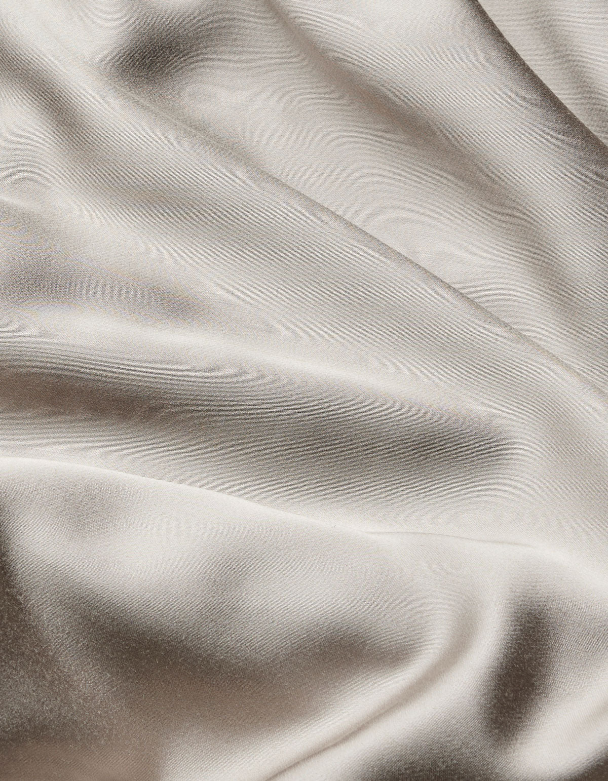 The Bamboo Flat Sheet by Cozy Earth features smooth, cream-colored satin fabric with gentle, flowing folds and a soft sheen that beautifully reflects light.|Color:Dove Grey