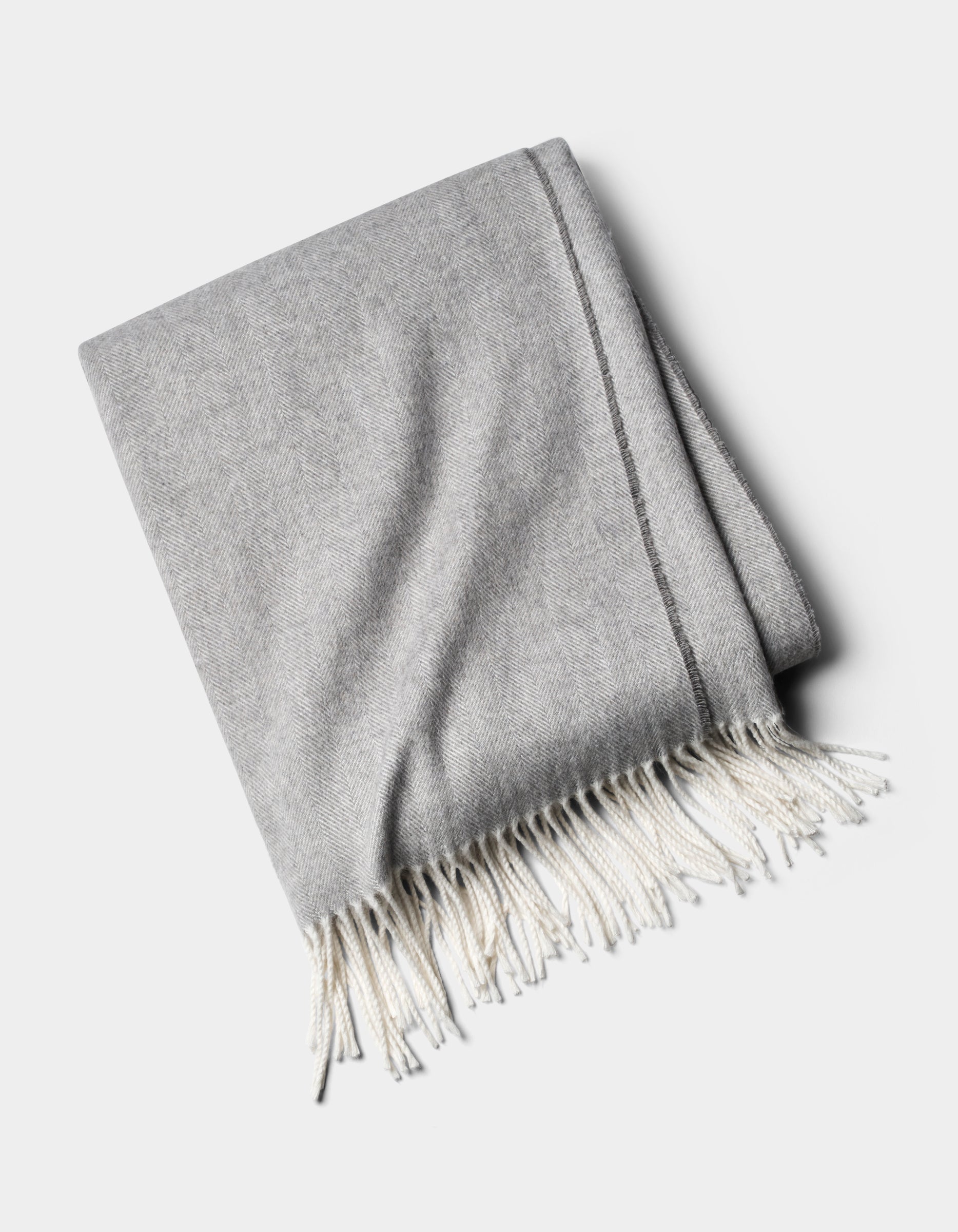 The Cozy Earth Bamboo Herringbone Tassel Throw is a folded light gray blanket with white fringed tassels on one edge, shown against a plain white background.|Color:Cloud
