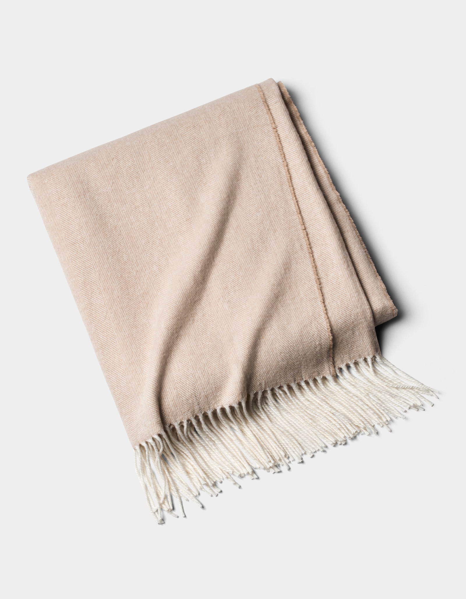 The Cozy Earth Bamboo Herringbone Tassel Throw, a beige blanket with white fringed edges, is shown folded on a plain white background.