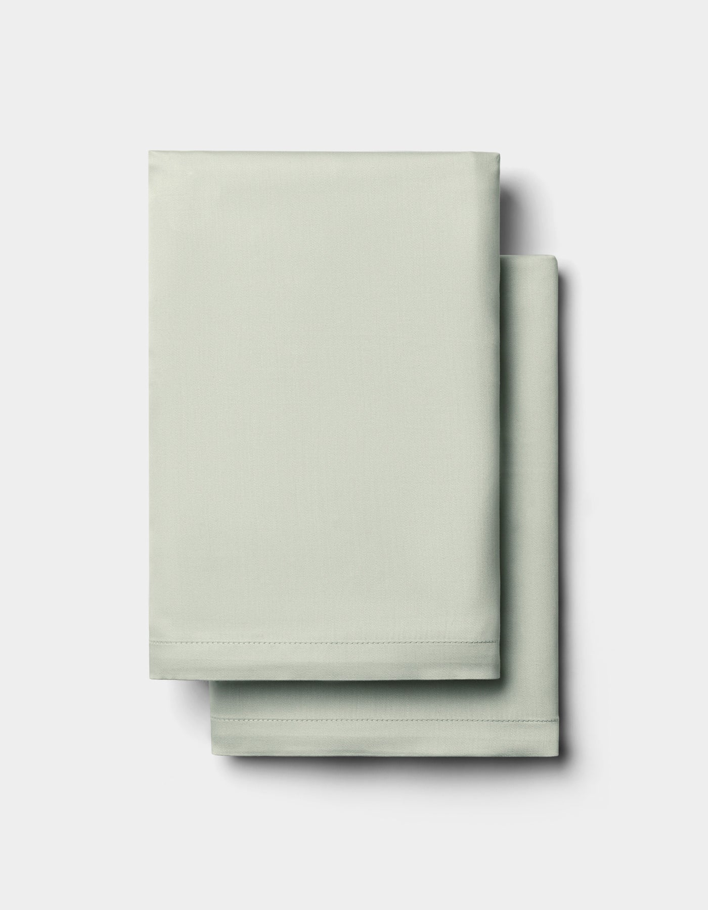 Two neatly folded Cozy Earth Bamboo Pillowcases in light green are stacked on top of each other against a plain white background.|Color:Laurel