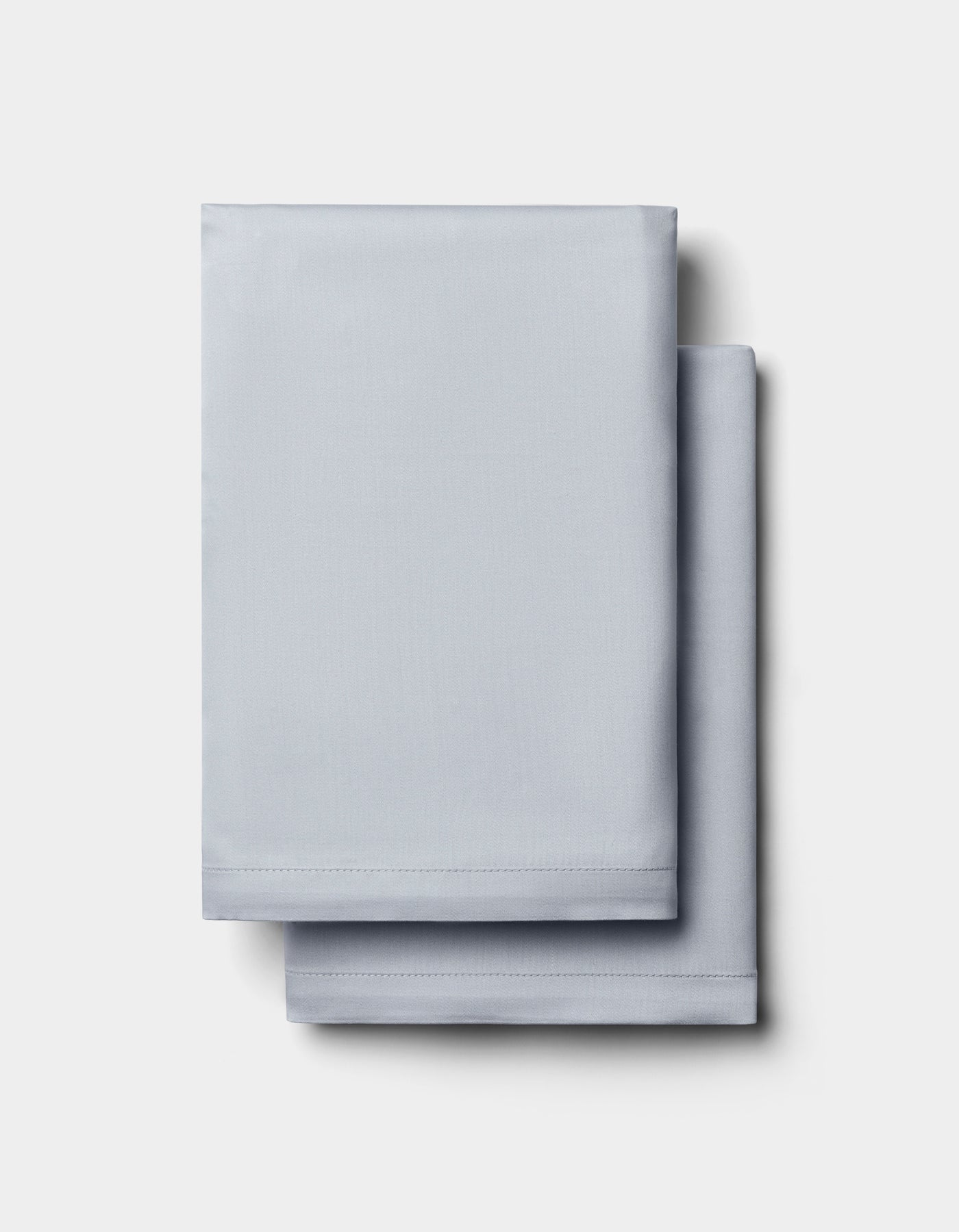 Two neatly folded Cozy Earth Bamboo Pillowcases in light gray are stacked on a plain white background.|Color:Shore