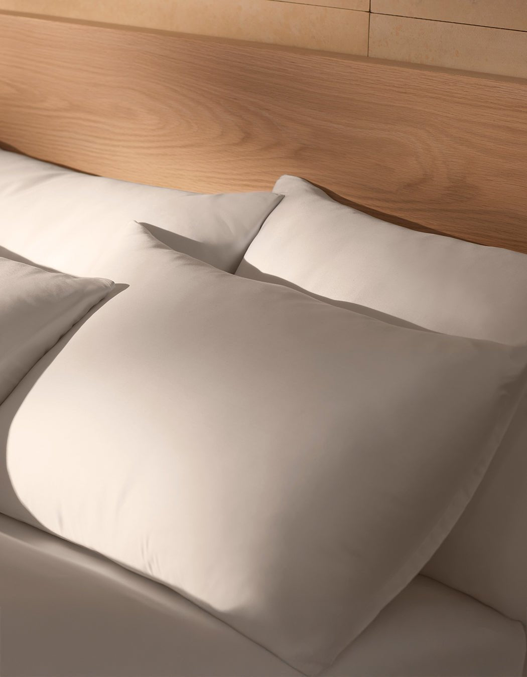 A close-up of a neatly made bed features two large Cozy Earth Bamboo Pillowcases against a wooden headboard, softly illuminated by natural light.