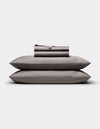 The Cozy Earth Bamboo Sheet Set, in dark gray, is neatly folded with matching pillowcases stacked atop two pillows, all arranged against a plain white background.|Color:Charcoal