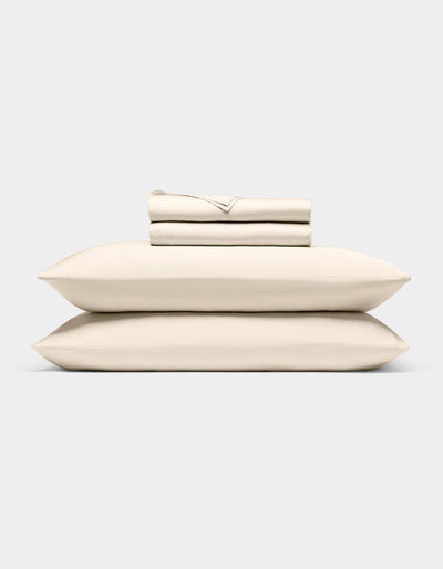 The Cozy Earth Bamboo Sheet Set, neatly folded in cream, rests atop two matching pillows against a light gray background.|Color:Creme