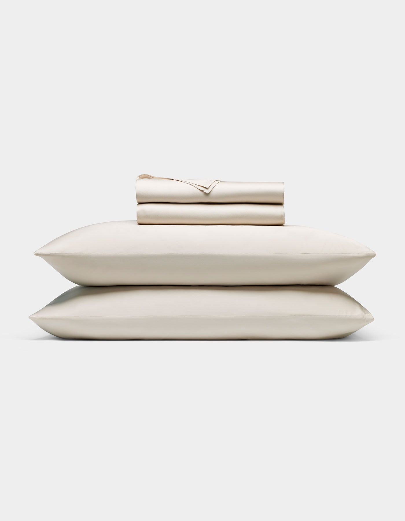 A neatly folded Cozy Earth Bamboo Sheet Set—cream-colored, including a fitted sheet, flat sheet, and two pillowcases—rests atop two matching pillows against a plain white background.|Color:Oat