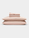 The Cozy Earth Bamboo Sheet Set in light pink is neatly folded with matching pillowcases, stacked on two pillows against a plain white background.|Color:Peony
