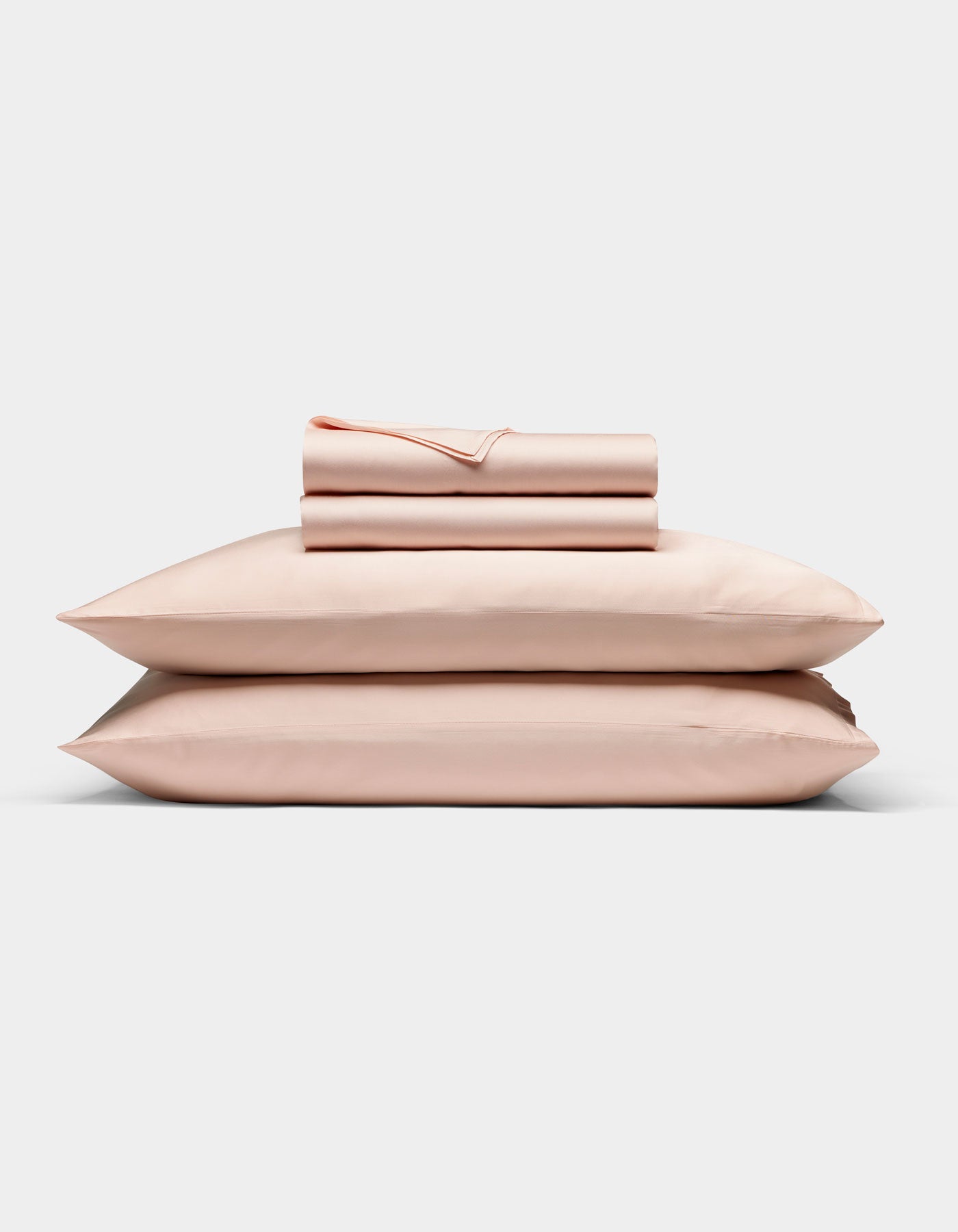 The Cozy Earth Bamboo Sheet Set in light pink is neatly folded with matching pillowcases, stacked on two pillows against a plain white background.|Color:Peony