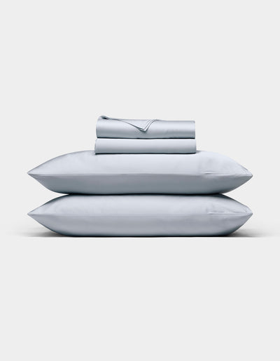 A neatly folded Cozy Earth Bamboo Sheet Set in light gray, with matching pillowcases stacked on two pillows, displayed against a plain white background.|Color:Shore