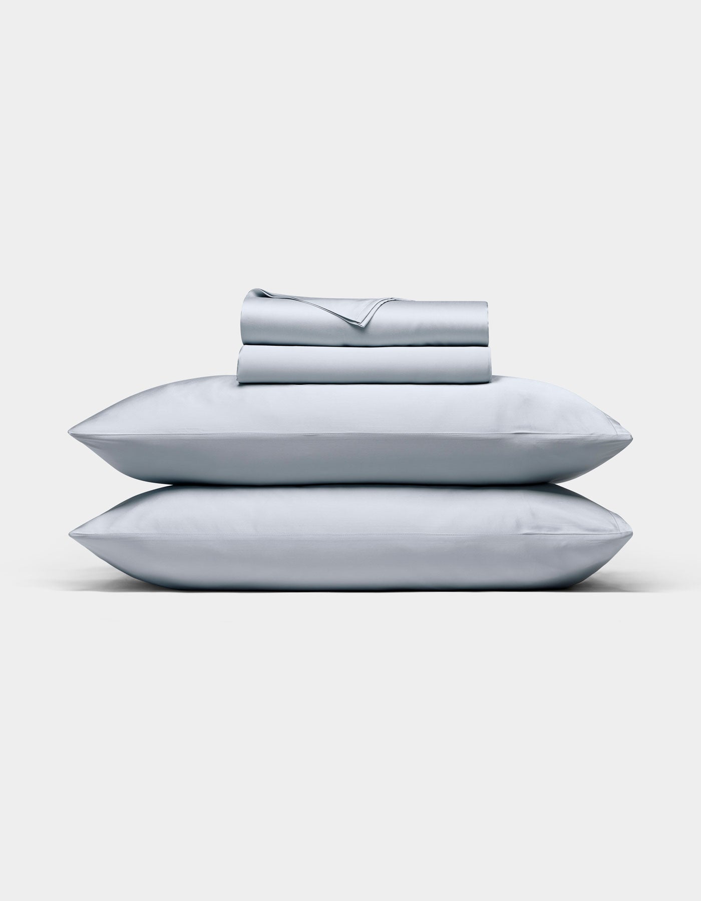 A neatly folded Cozy Earth Bamboo Sheet Set in light gray, with matching pillowcases stacked on two pillows, displayed against a plain white background.|Color:Shore