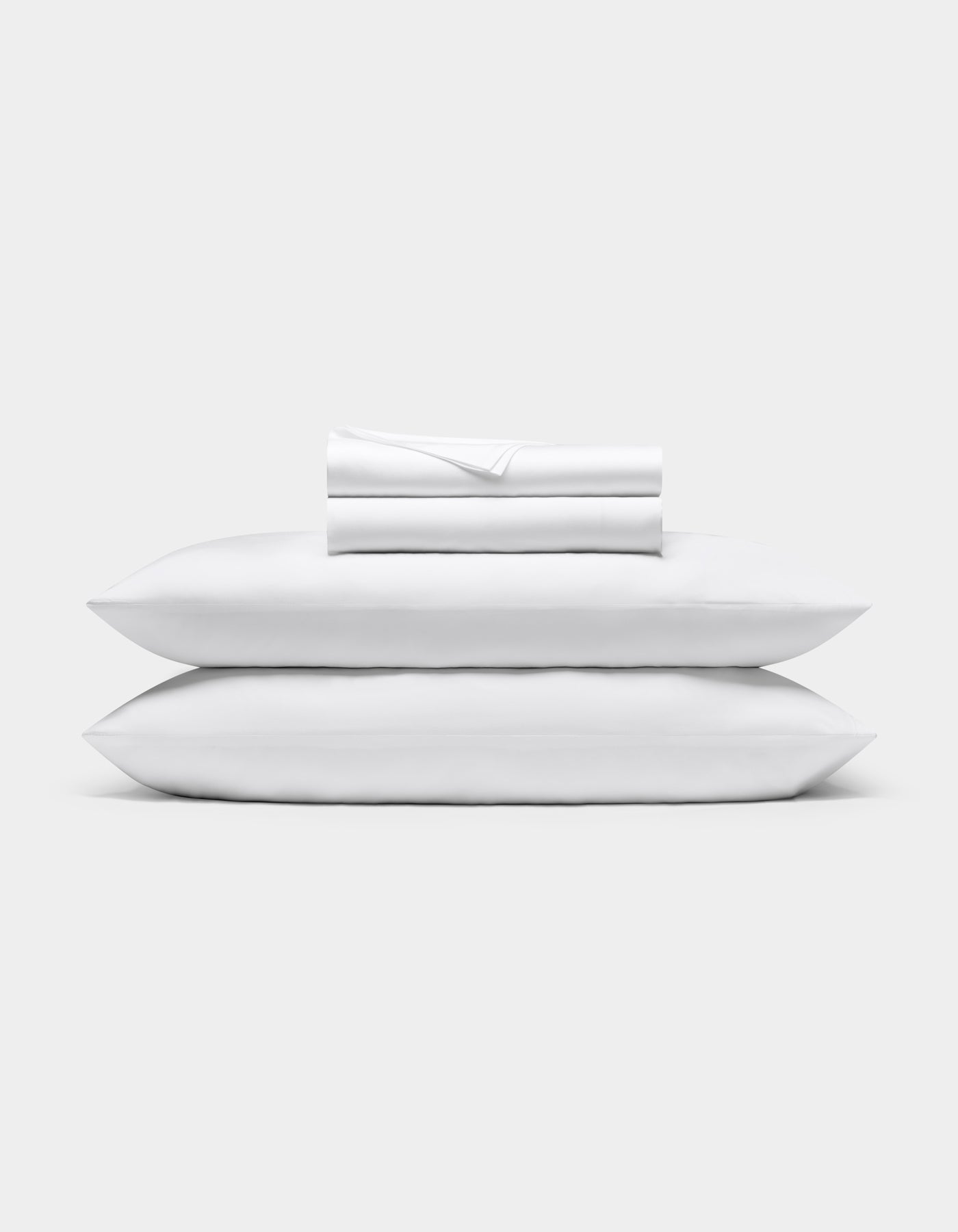 A neatly folded Bamboo Sheet Set by Cozy Earth is stacked on two white pillows, all set against a plain light gray background.|Color:White