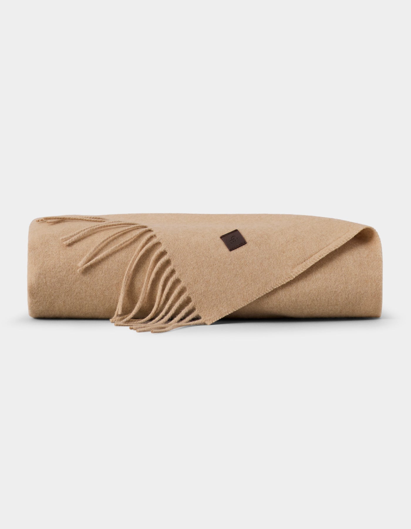 The Cozy Earth Cashmere Tassel Throw, a folded beige blanket with fringed edges and a small brown label, rests on a plain white background.|Color:Dune