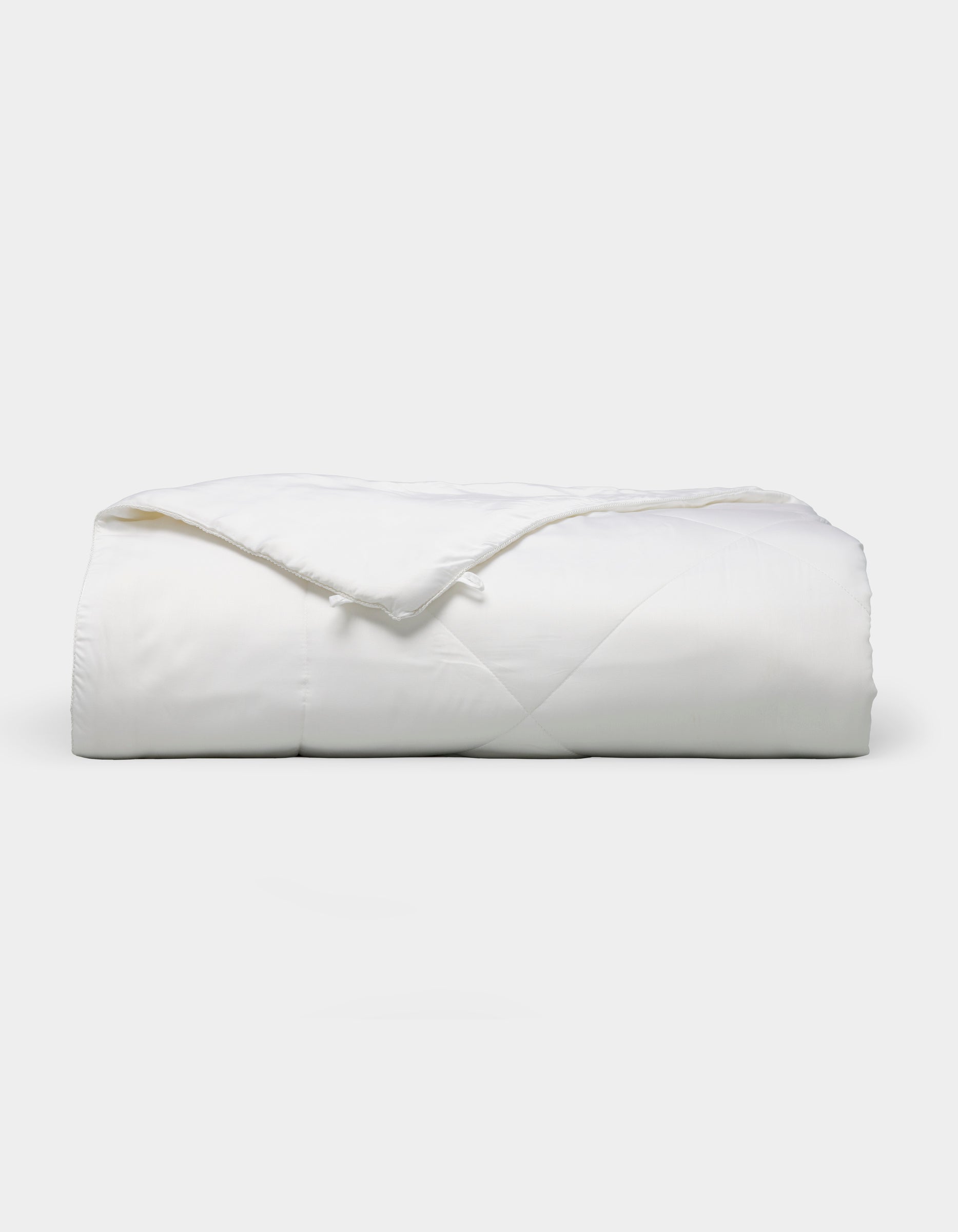 The Bamboo Viscose All Season Comforter by Cozy Earth, featuring a neatly folded white design with a subtle sheen, is displayed against a plain light background.