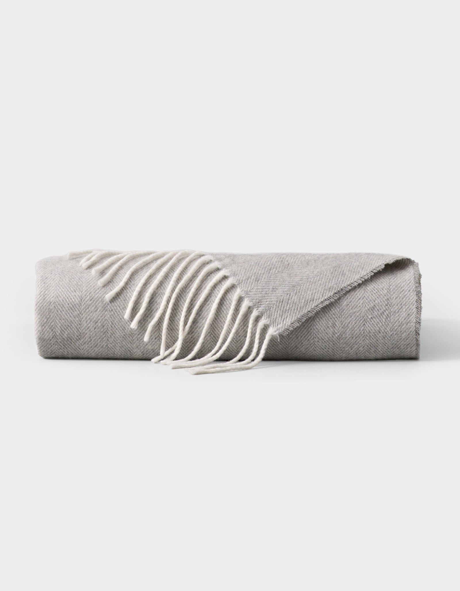 The Bamboo Herringbone Tassel Throw by Cozy Earth, featuring a light gray hue and white fringed edges, is neatly folded and displayed on a plain white background.