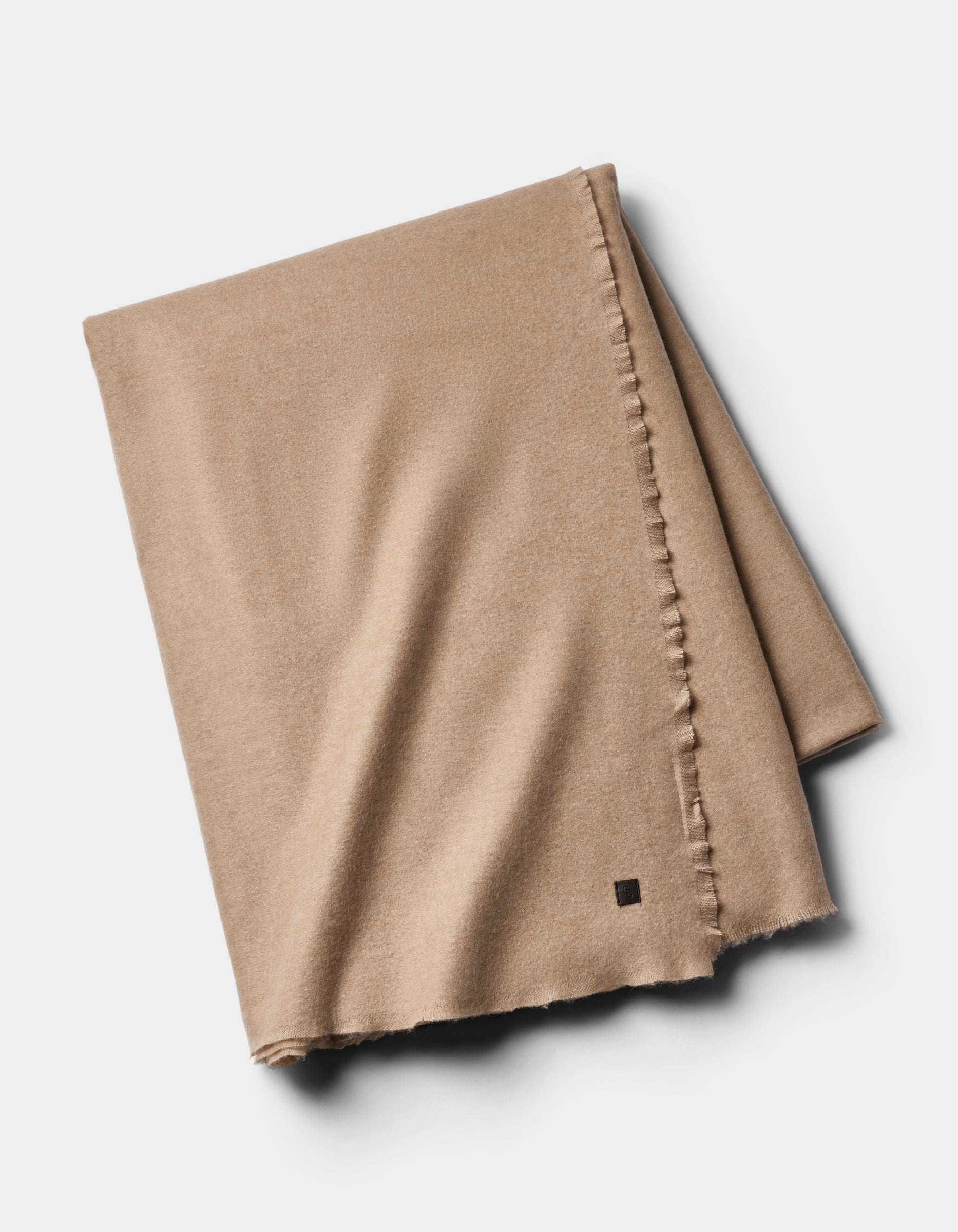 The Cozy Earth Cashmere Fringe Blanket in light brown, neatly folded with subtle frayed edges, lies on a plain white background.|Color:Dune