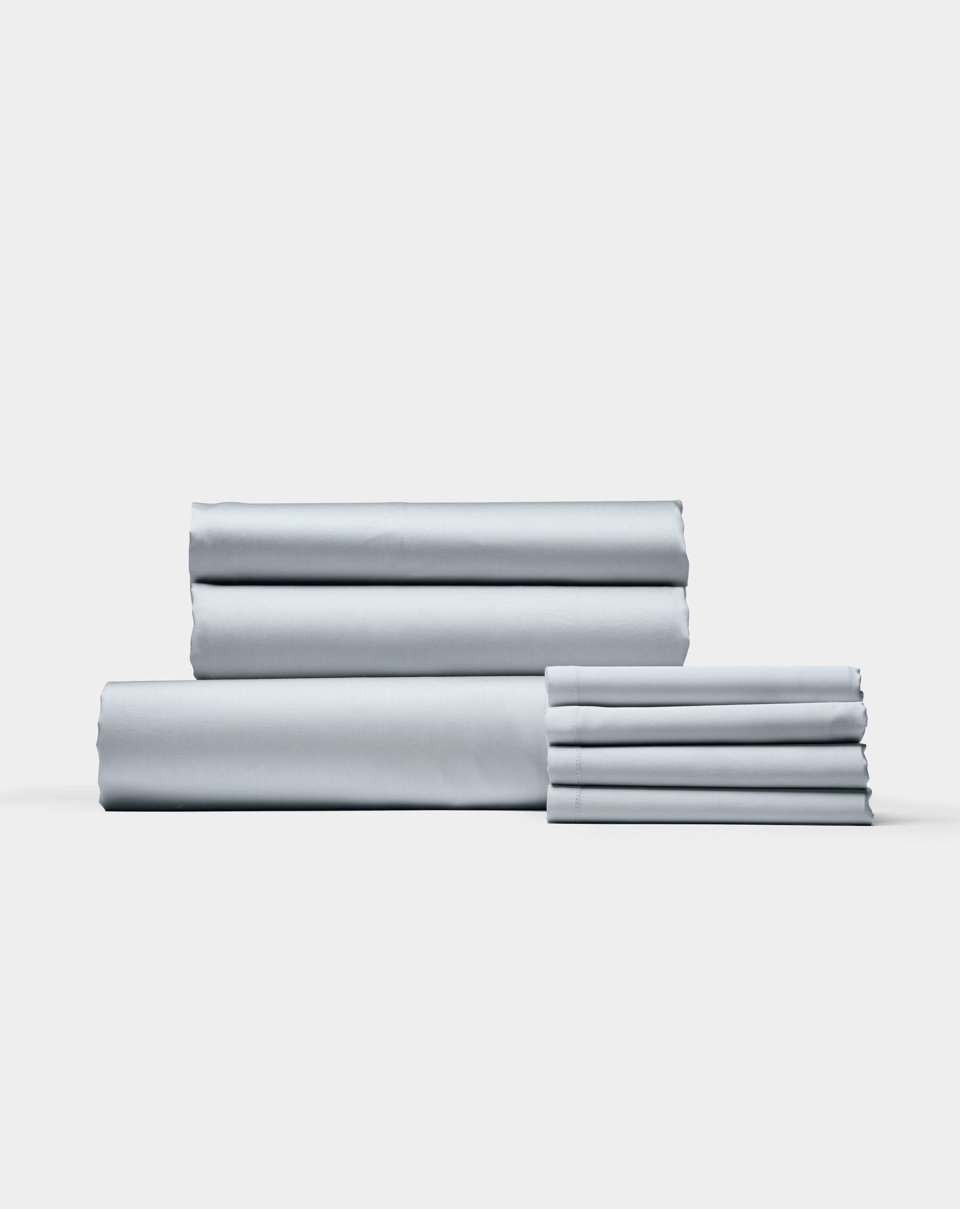 The Bamboo Bedding Core Bundle by Cozy Earth features neatly folded light gray bed sheets and pillowcases stacked against a plain white background.|Color:Shore