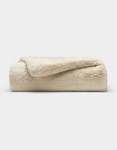 The Cozy Earth Cuddle Blanket, a plush cream-colored faux fur throw, is neatly folded and displayed against a plain white background.|Color:Creme