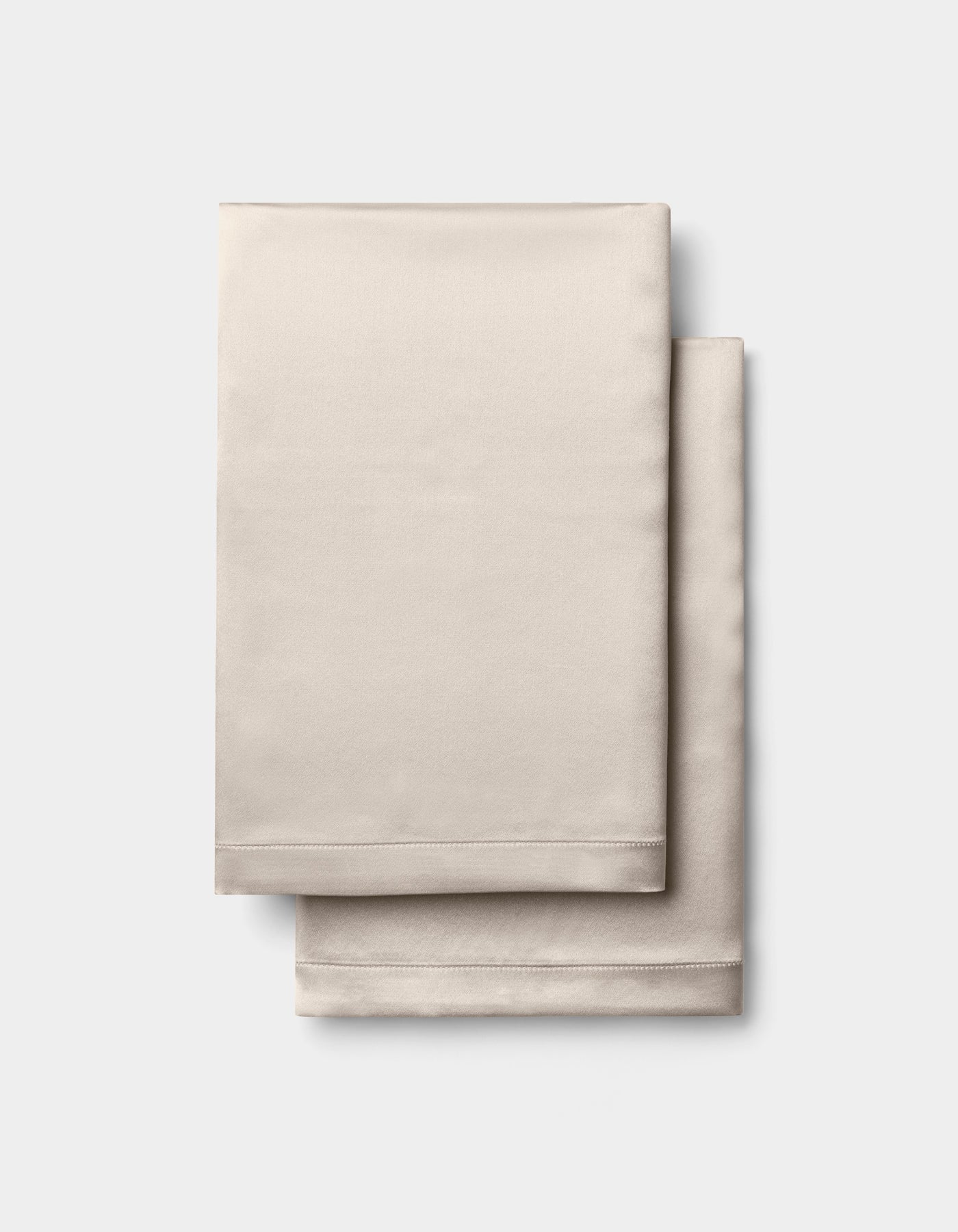Two neatly folded Cozy Earth Silk Pillowcases in beige, stacked together against a plain white background.|Color:Driftwood